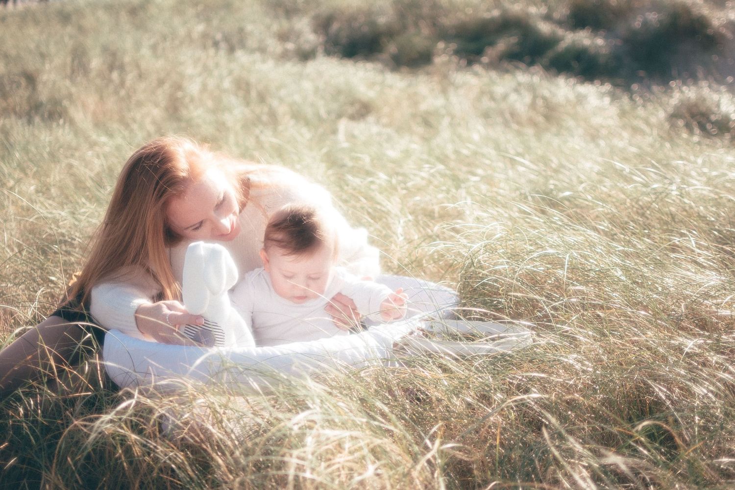 Mère allongée dans les hautes herbes tenant son bébé, moment de tendresse et lumière naturelle à Pen Bron