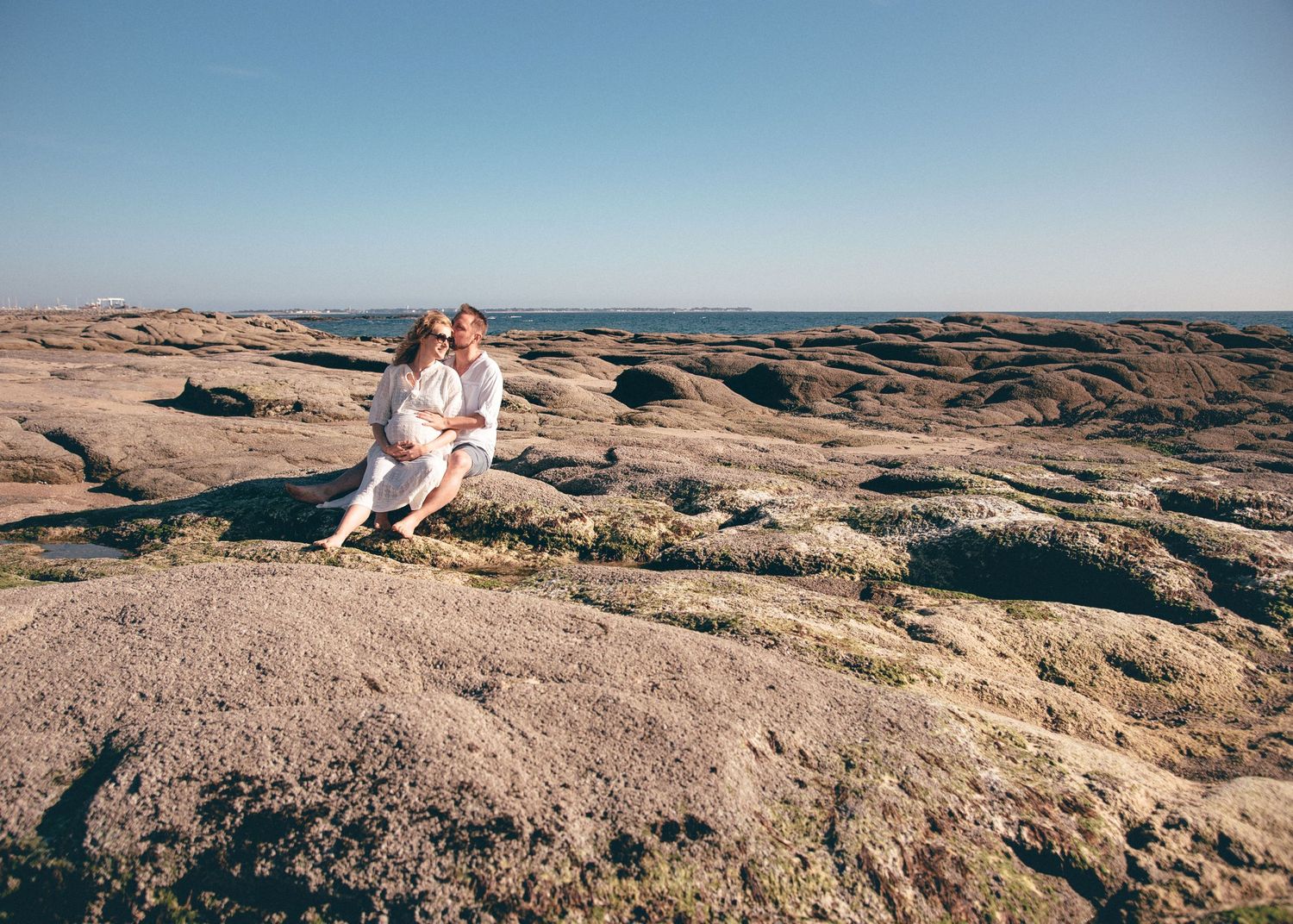 Femme enceinte et futur papa assis face à la mer, photographie de maternité en lumière naturelle à La Turballe