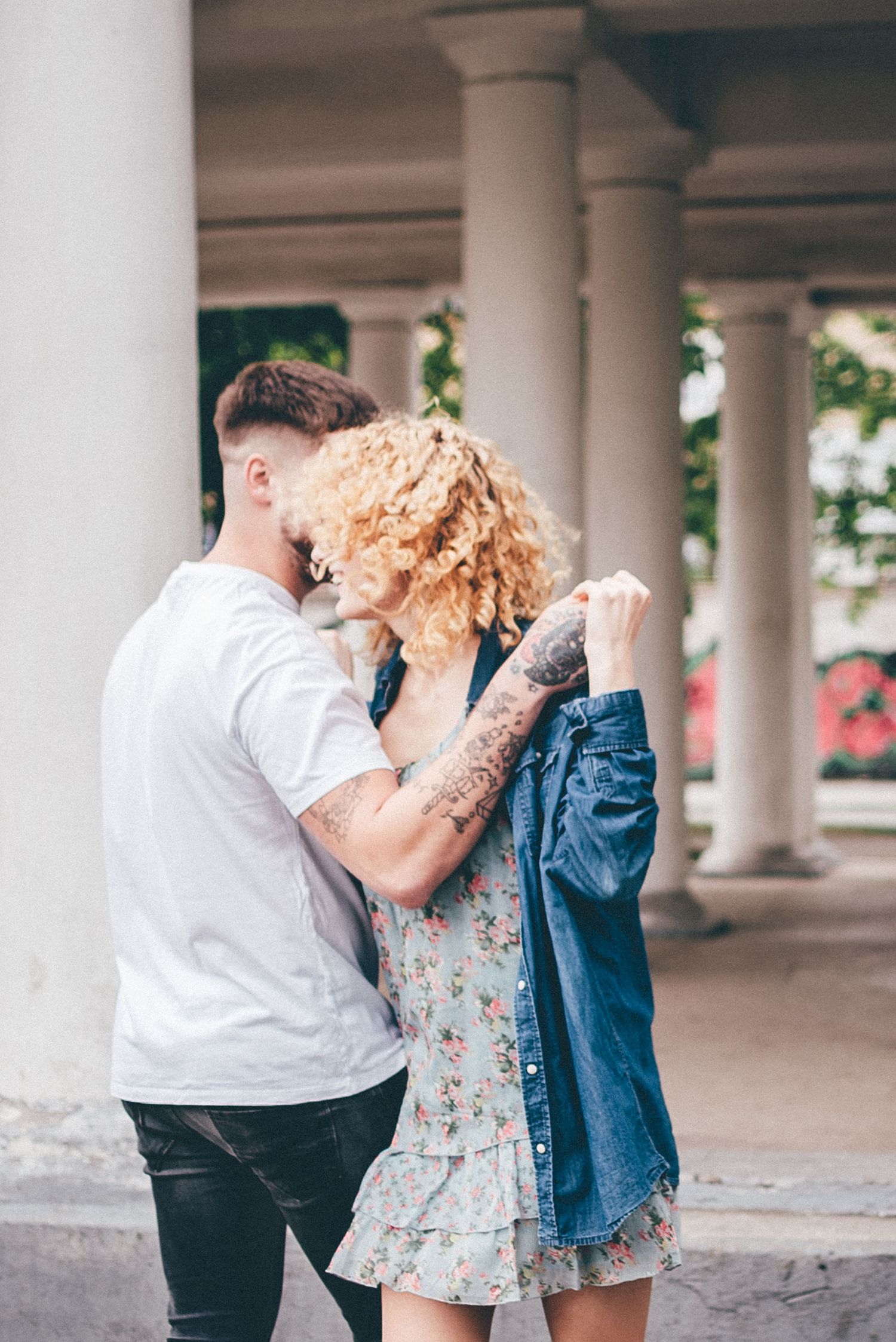 Couple sharing intimate moment under architectural columns outdoors.
