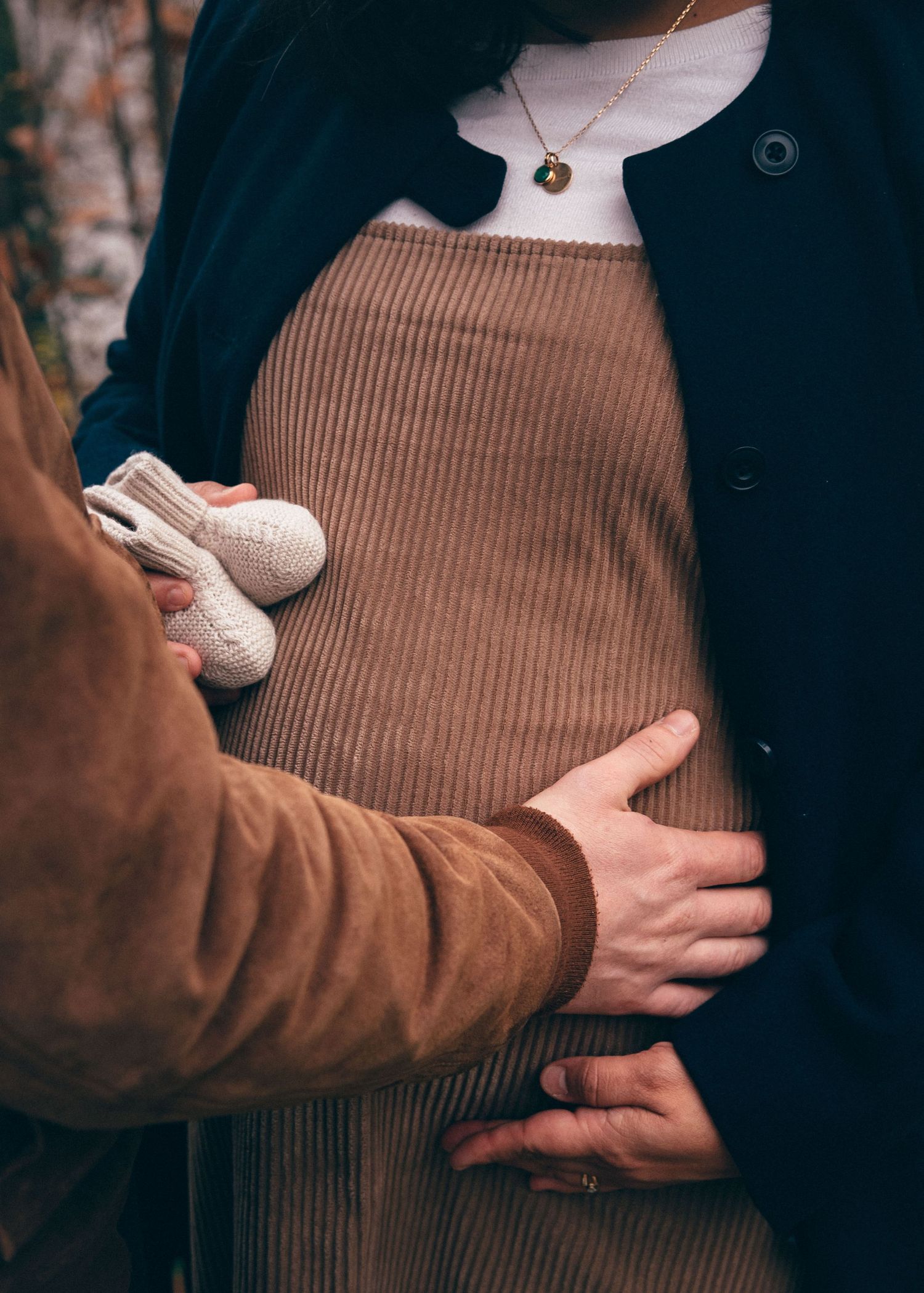 Détail d’un ventre de femme enceinte entouré par les mains des futurs parents, séance photo grossesse au parc de la Chantrerie à Nantes