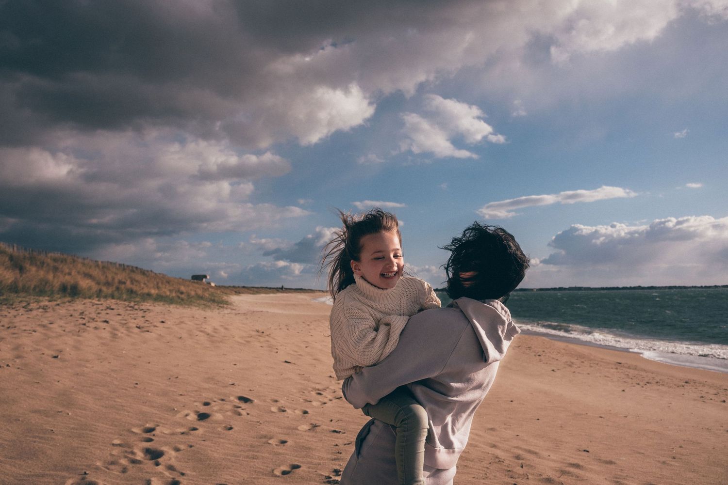 Parent portant son enfant sur la plage de La Turballe, instant de complicité face à l’océan