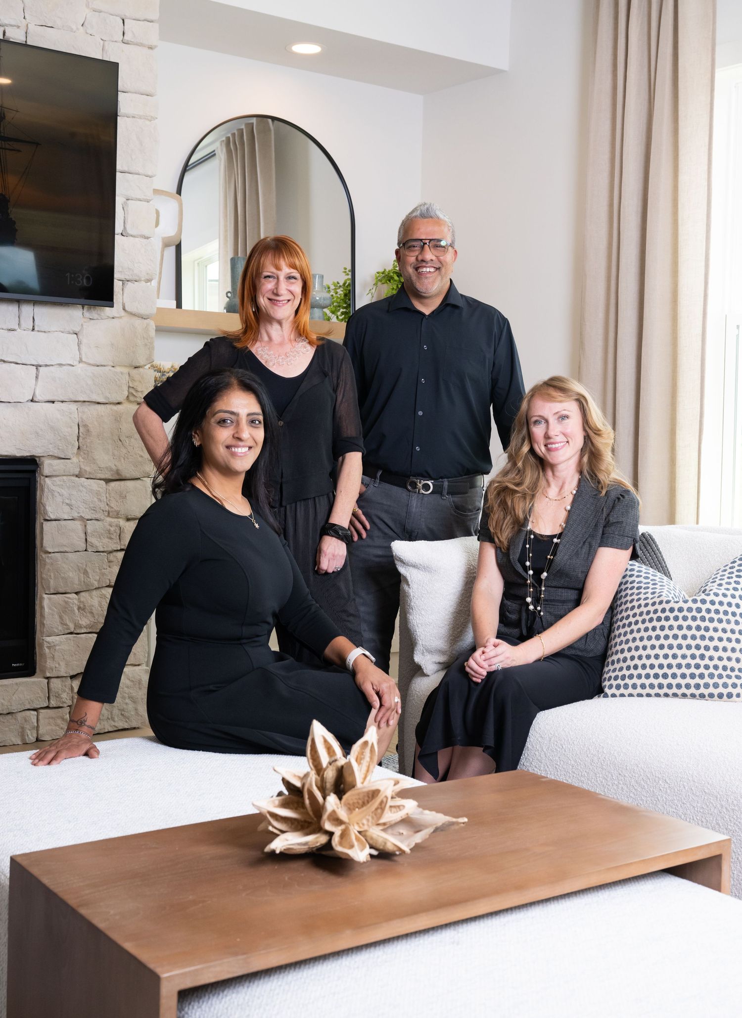 Professional group photo of four realtors in business attire sitting and standing in a modern living room with white decor.