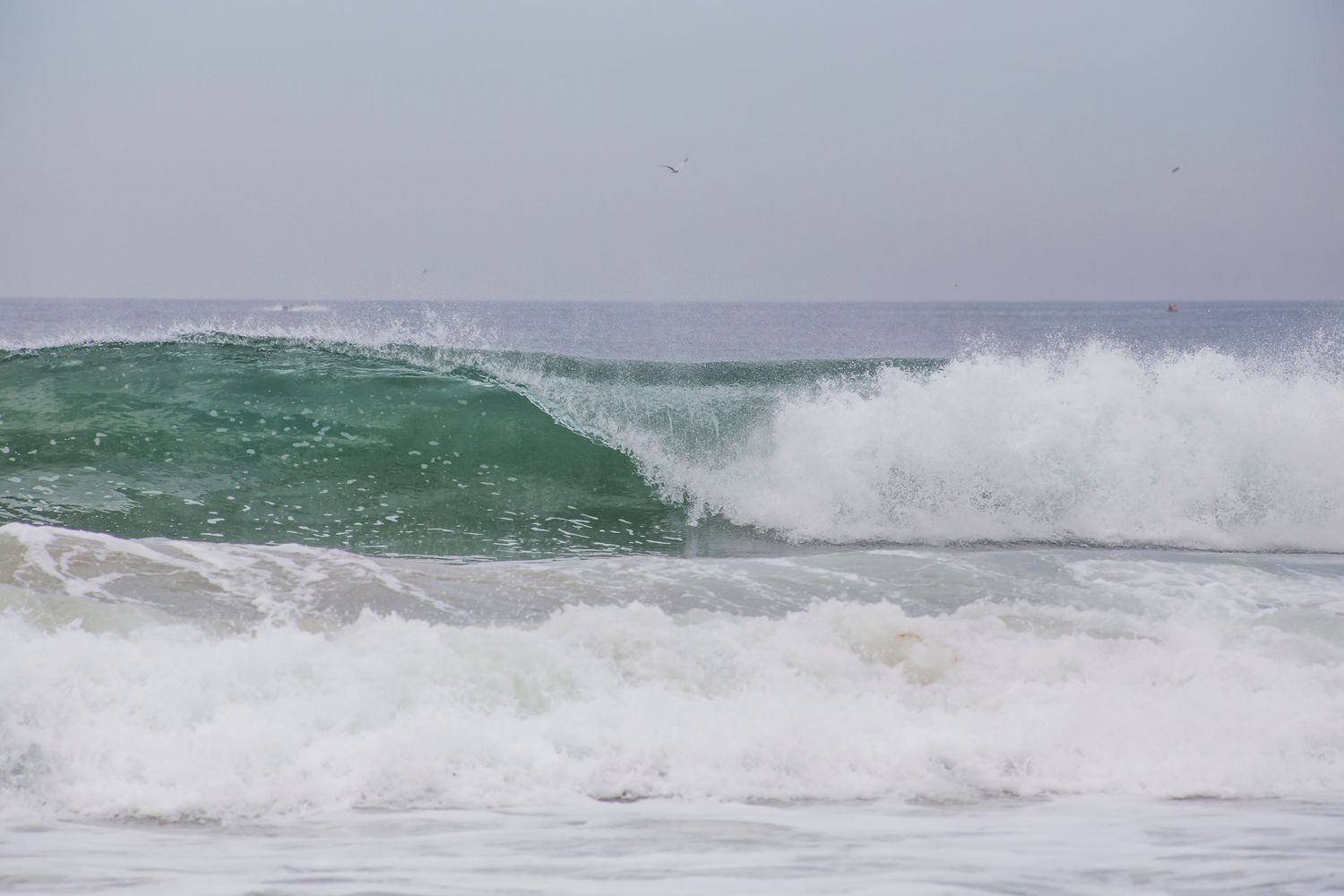 A powerful ocean wave curls with emerald green water and white spray breaking against the misty seascape.