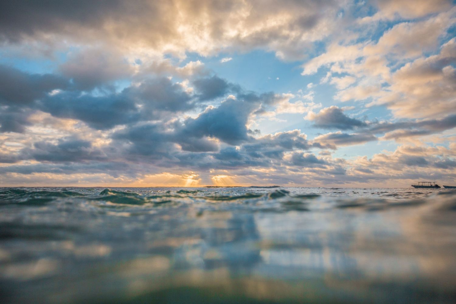 Dramatic panoramic sunset over an ocean lagoon with vibrant clouds reflecting in calm waters.
