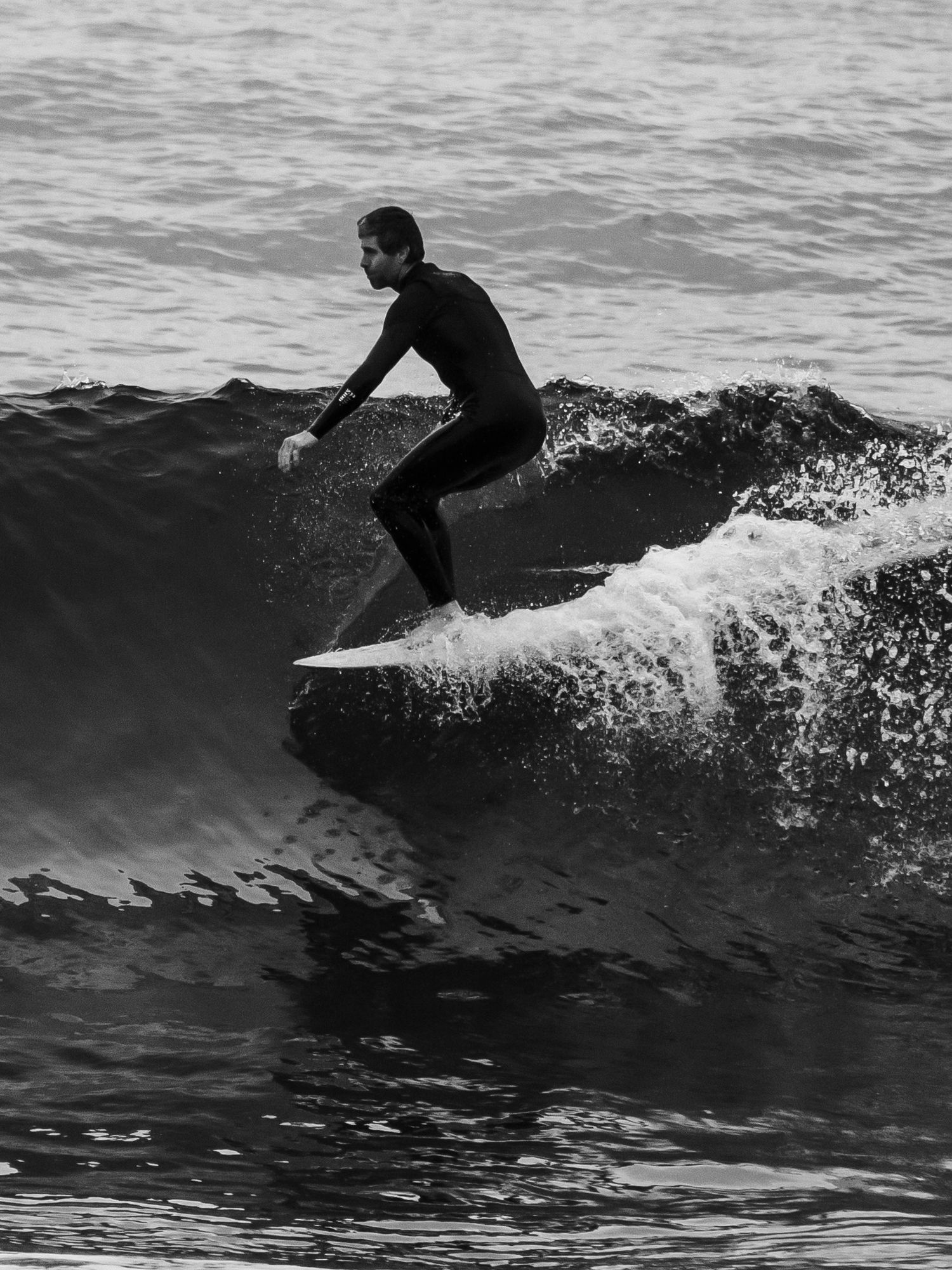 A surfer rides a dark wave in black and white silhouette against a moody ocean backdrop.