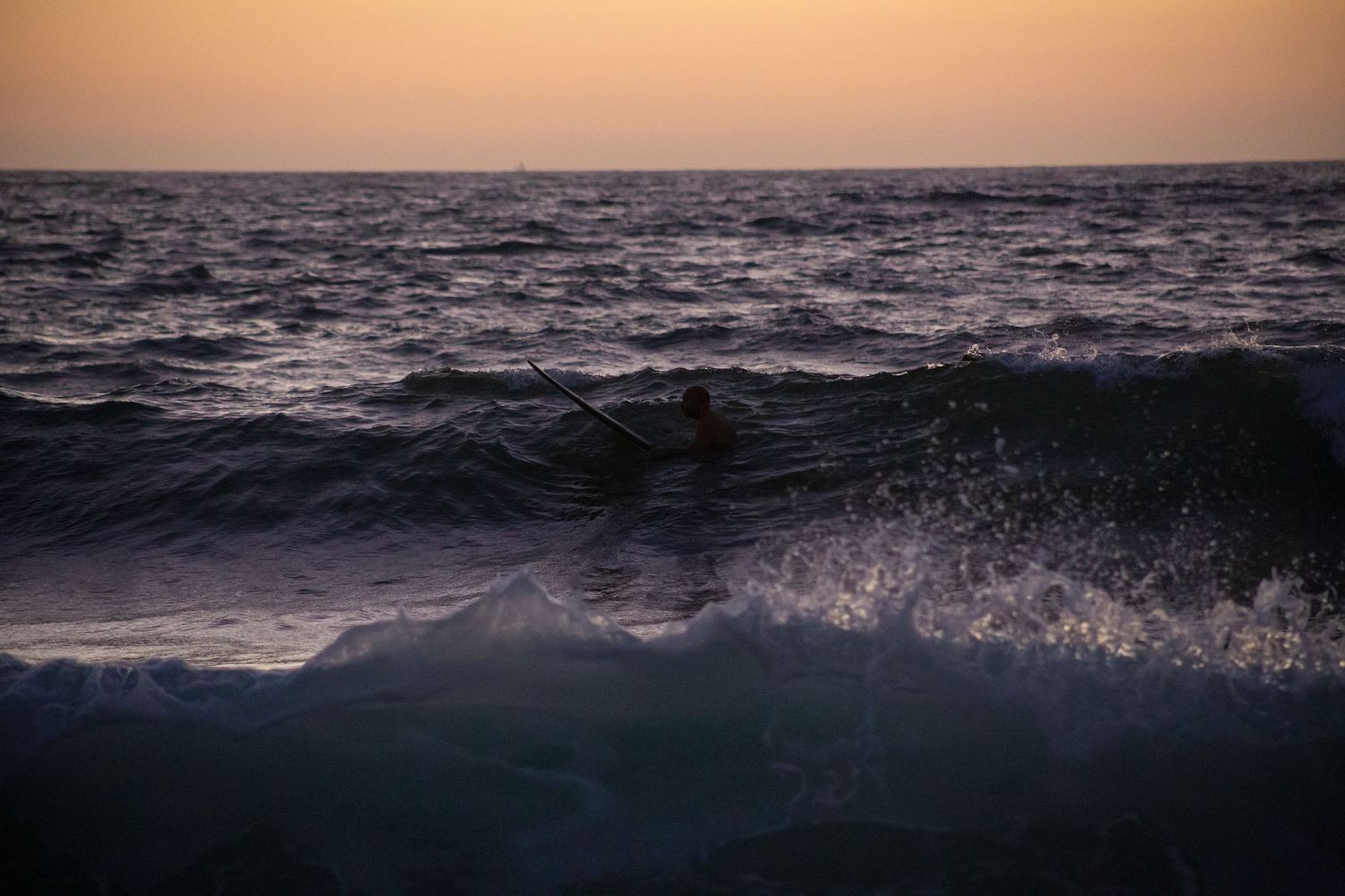 Scenic sunset over ocean waves with warm orange glow reflecting on the rippling water surface.