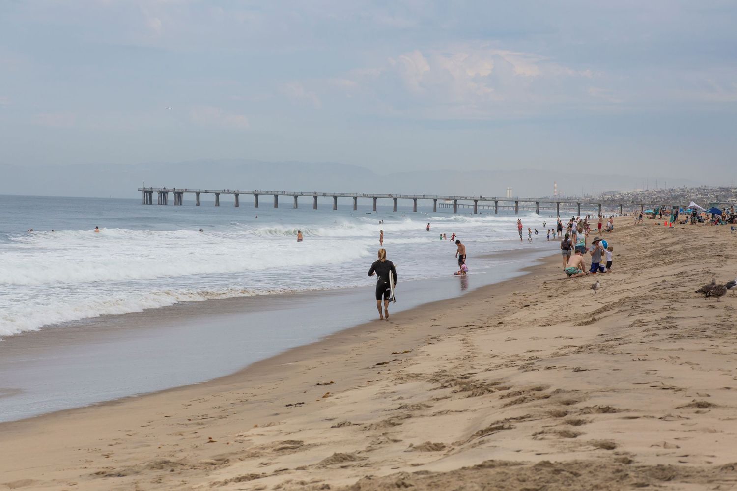Surfer enjoying a sunny day at Hermosa Beach pier with waves crashing on the sandy shore.