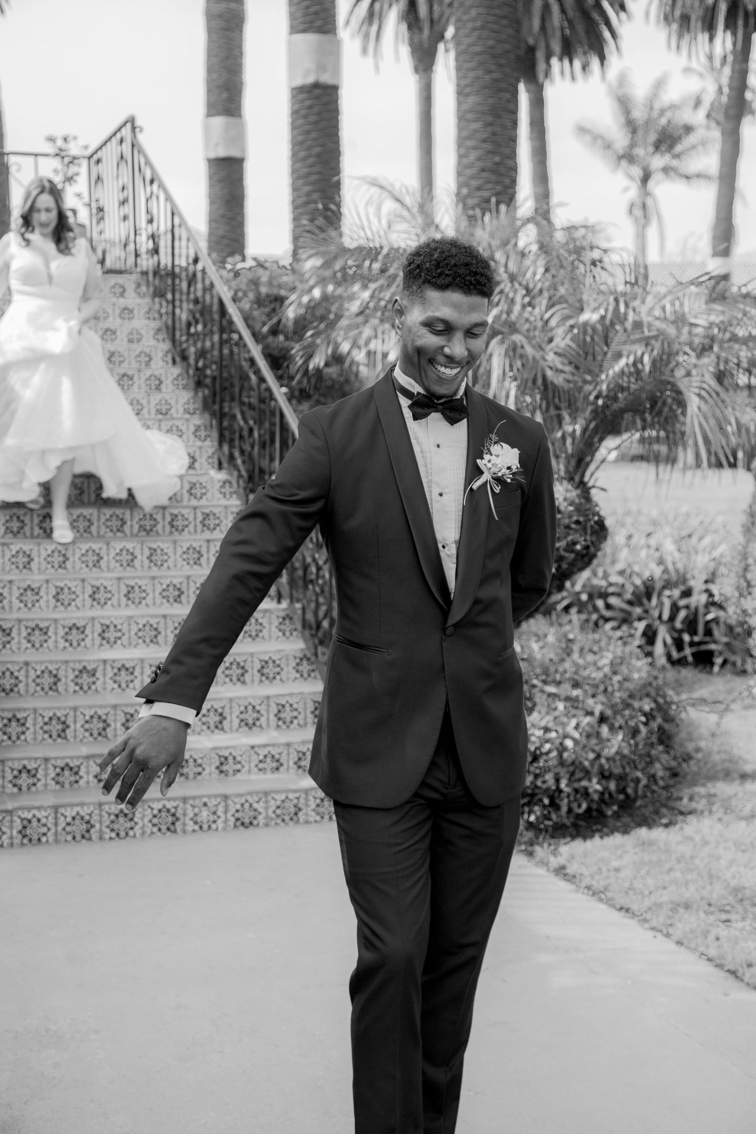 A groom in a dark suit strikes playful poses in a series of black and white photos outdoors near palm trees for his bride.
