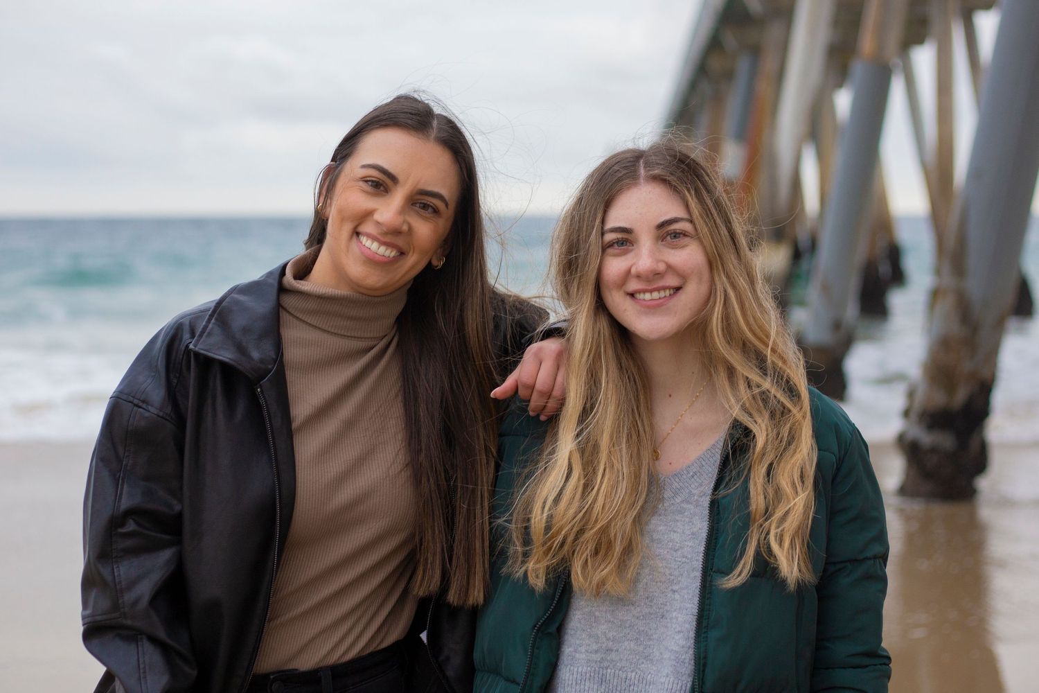 Two friends poses together in multiple candid shots along a beach pier during a beach photoshoot session.