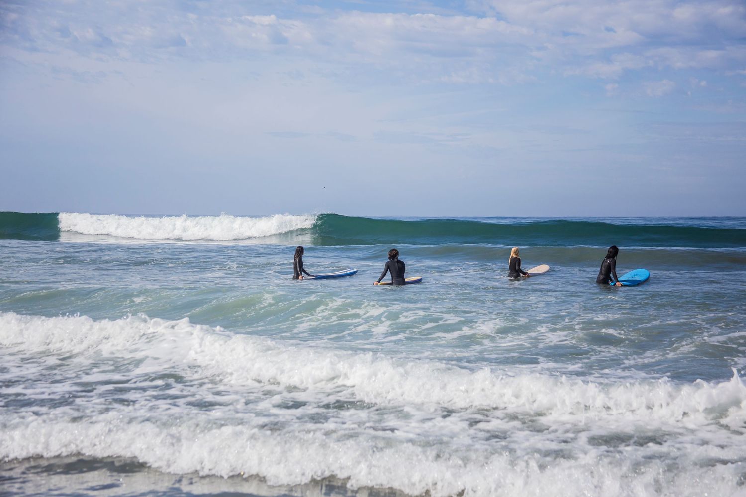 All women surfers paddle out into rolling ocean waves on a cloudy day at the beach.