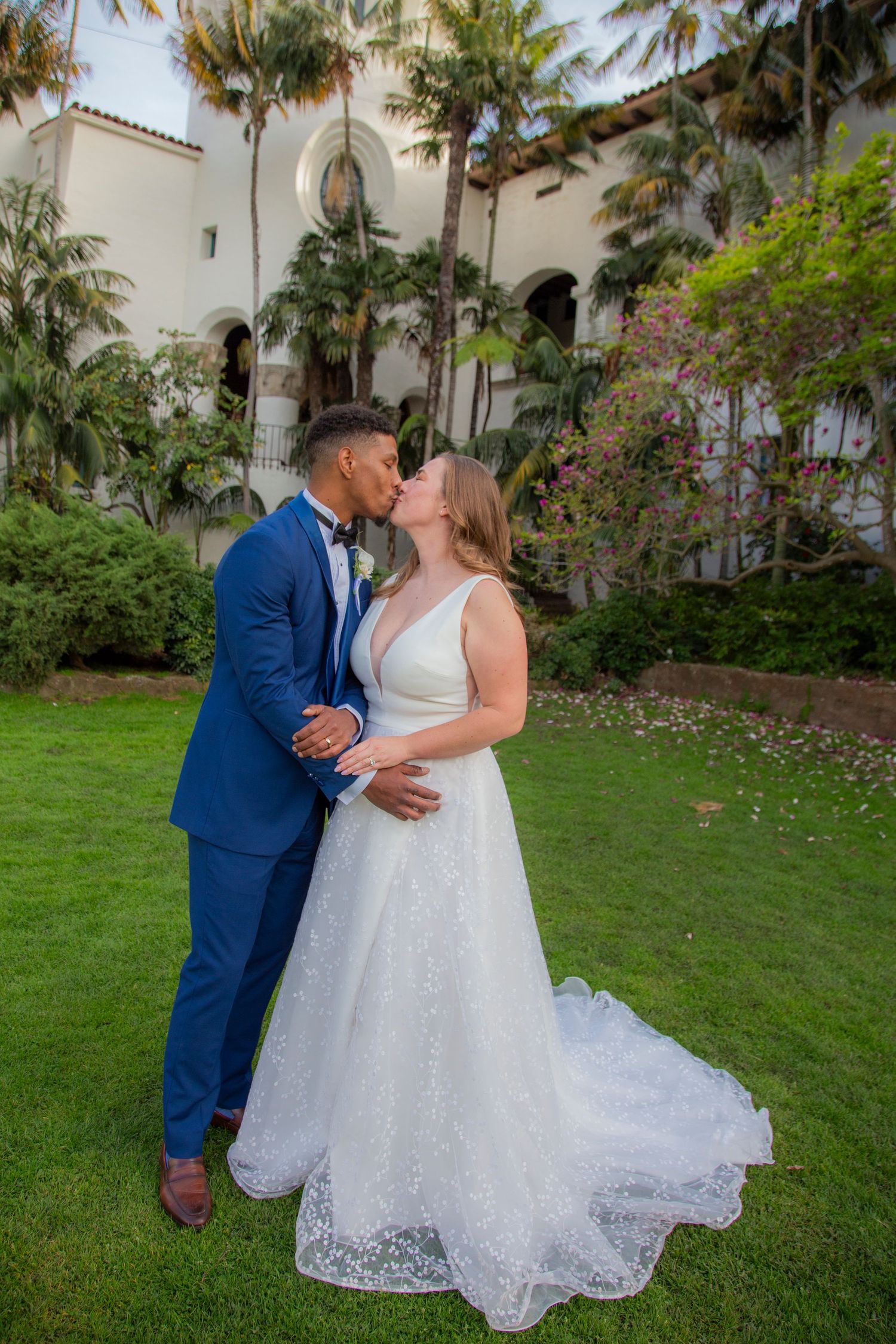 A romantic wedding couple shares a tender moment on a lush green lawn with palm trees and Spanish architecture in Santa Barbara, California.