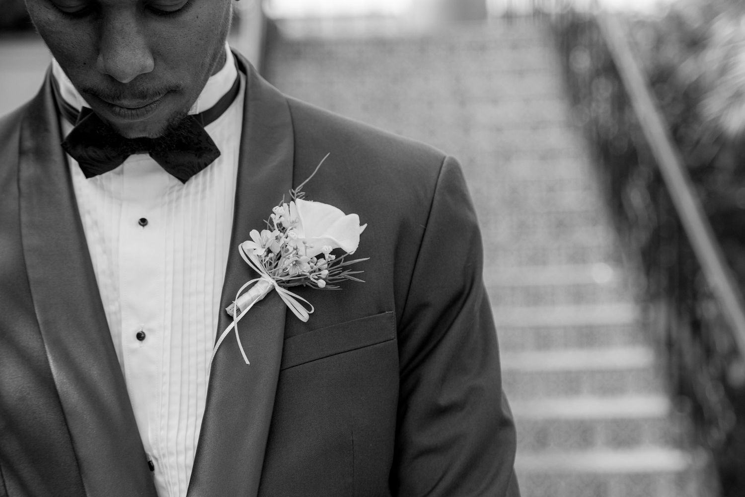 Groom in formal black tuxedo and bow tie stands waiting for his bride during first look wedding photo.