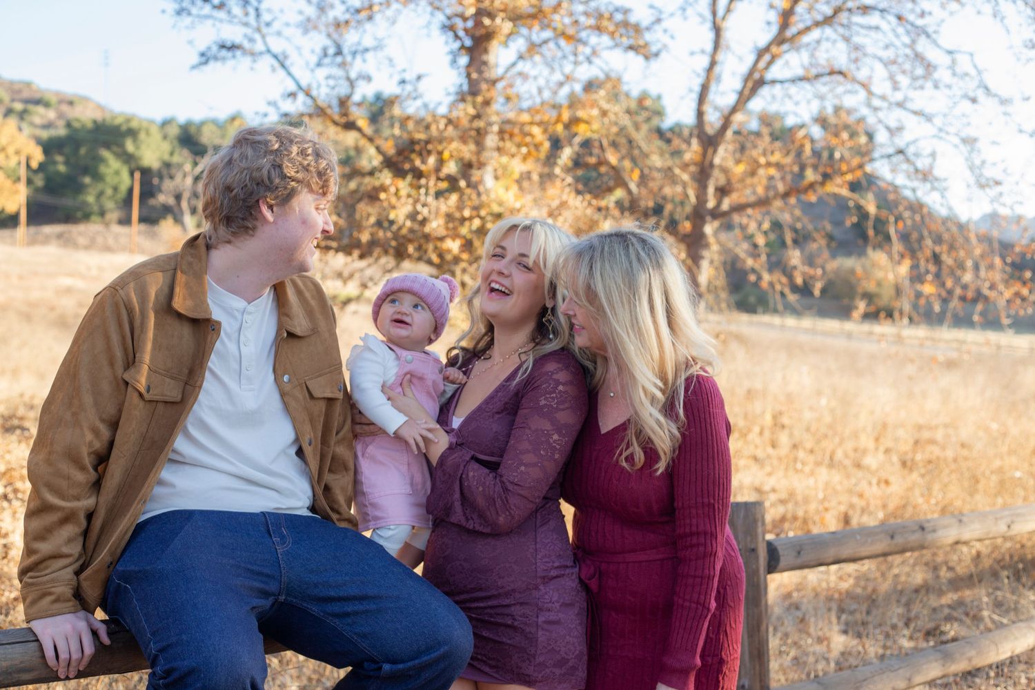 A family enjoys a candid moment together while sitting outdoors during golden hour in autumn.