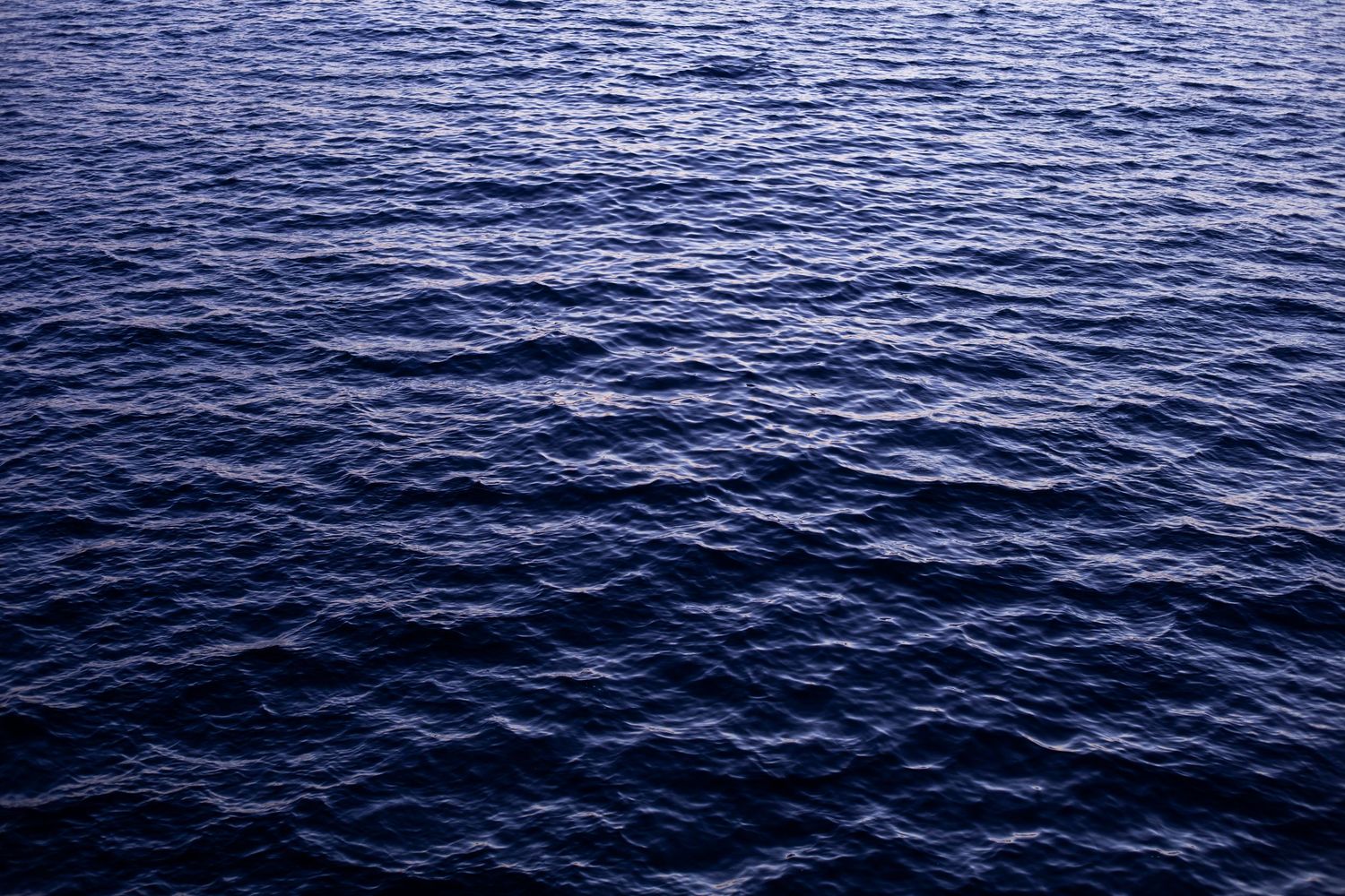 Dark blue ocean waves ripple across a vast seascape under overcast skies creating a moody maritime atmosphere.