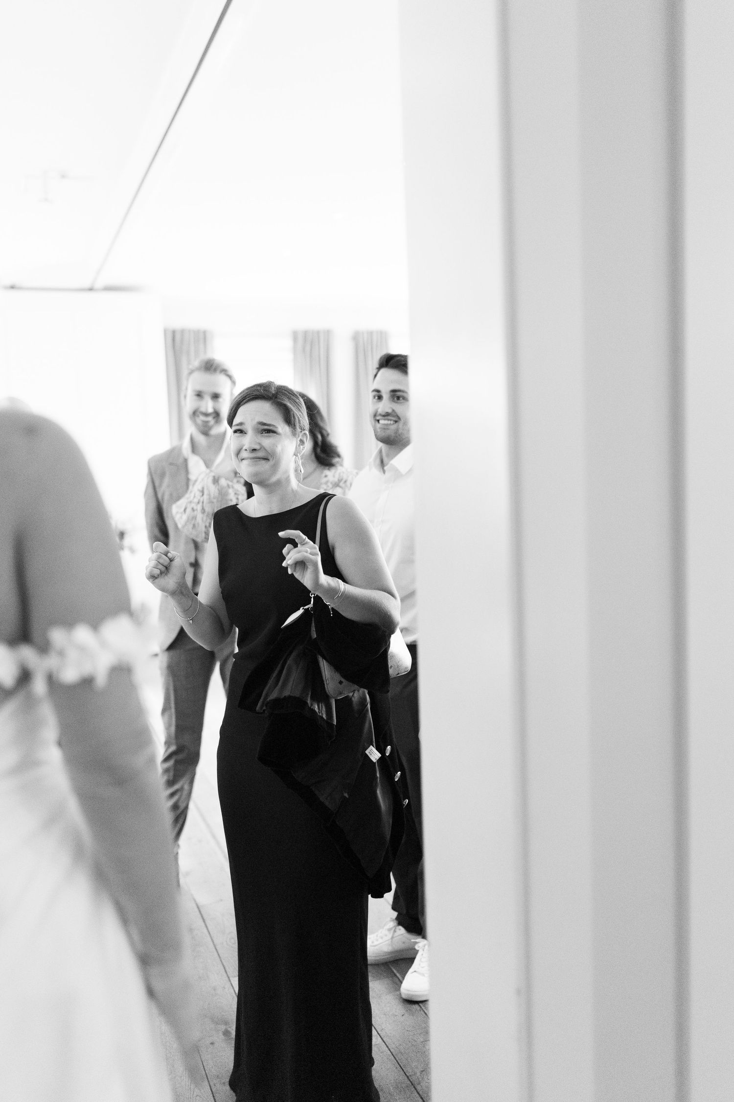 Black and white photo of wedding guests smiling as they see the bride in her gown during bridal preparations.