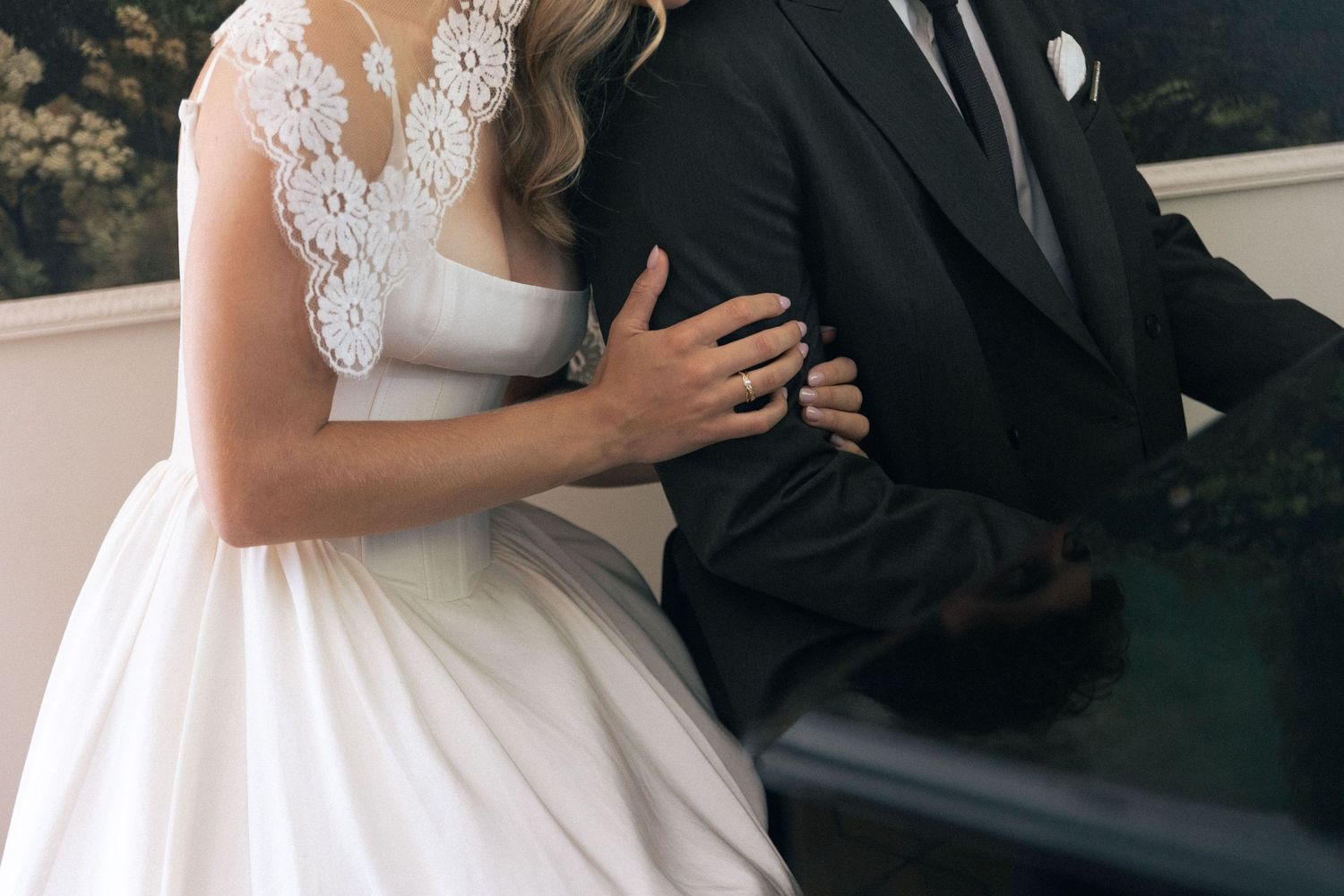 Bride in lace wedding gown and groom in black suit embrace closely during elegant wedding ceremony.