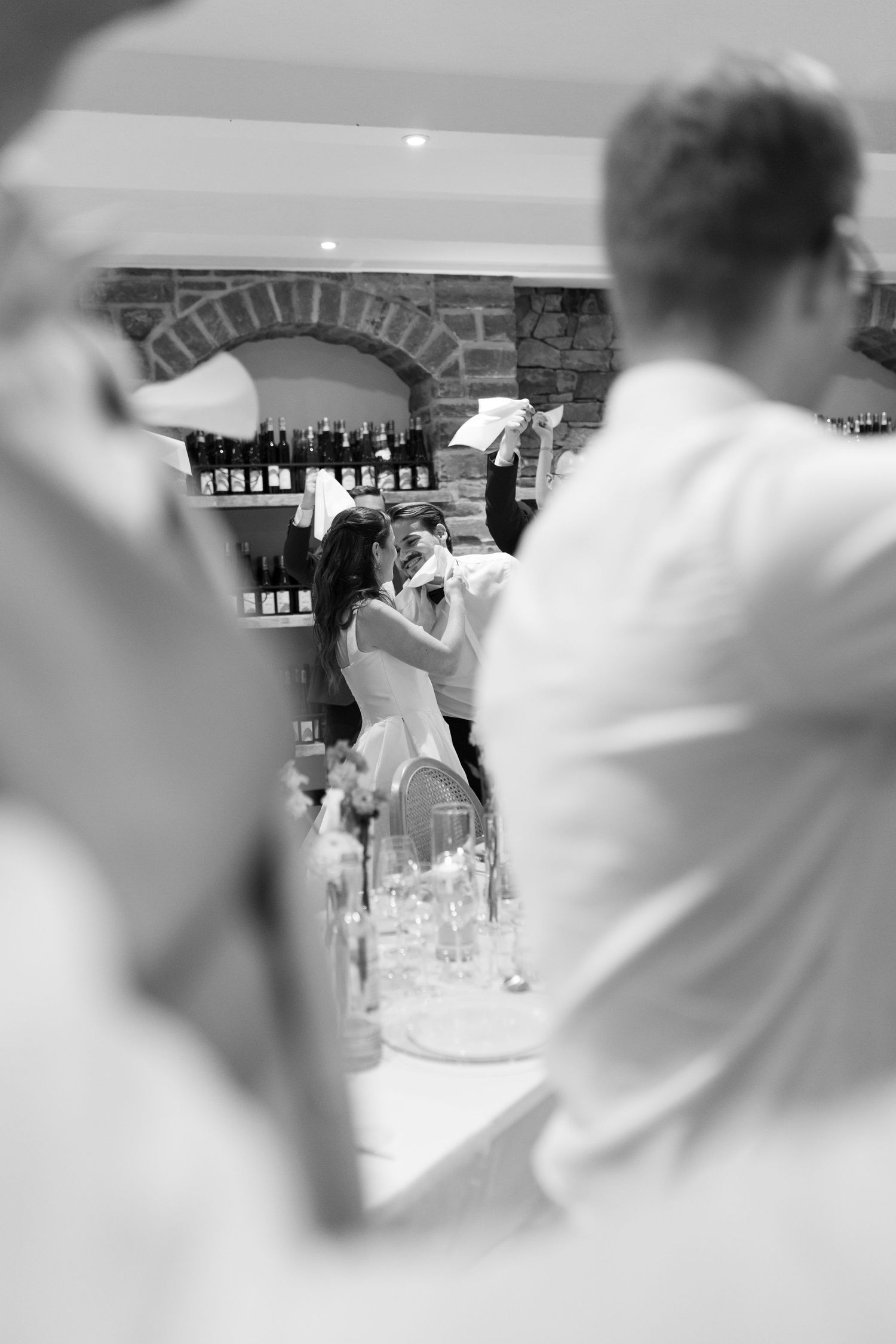 Black and white photo of a couple sharing a kiss at their wedding reception near a wine bar.