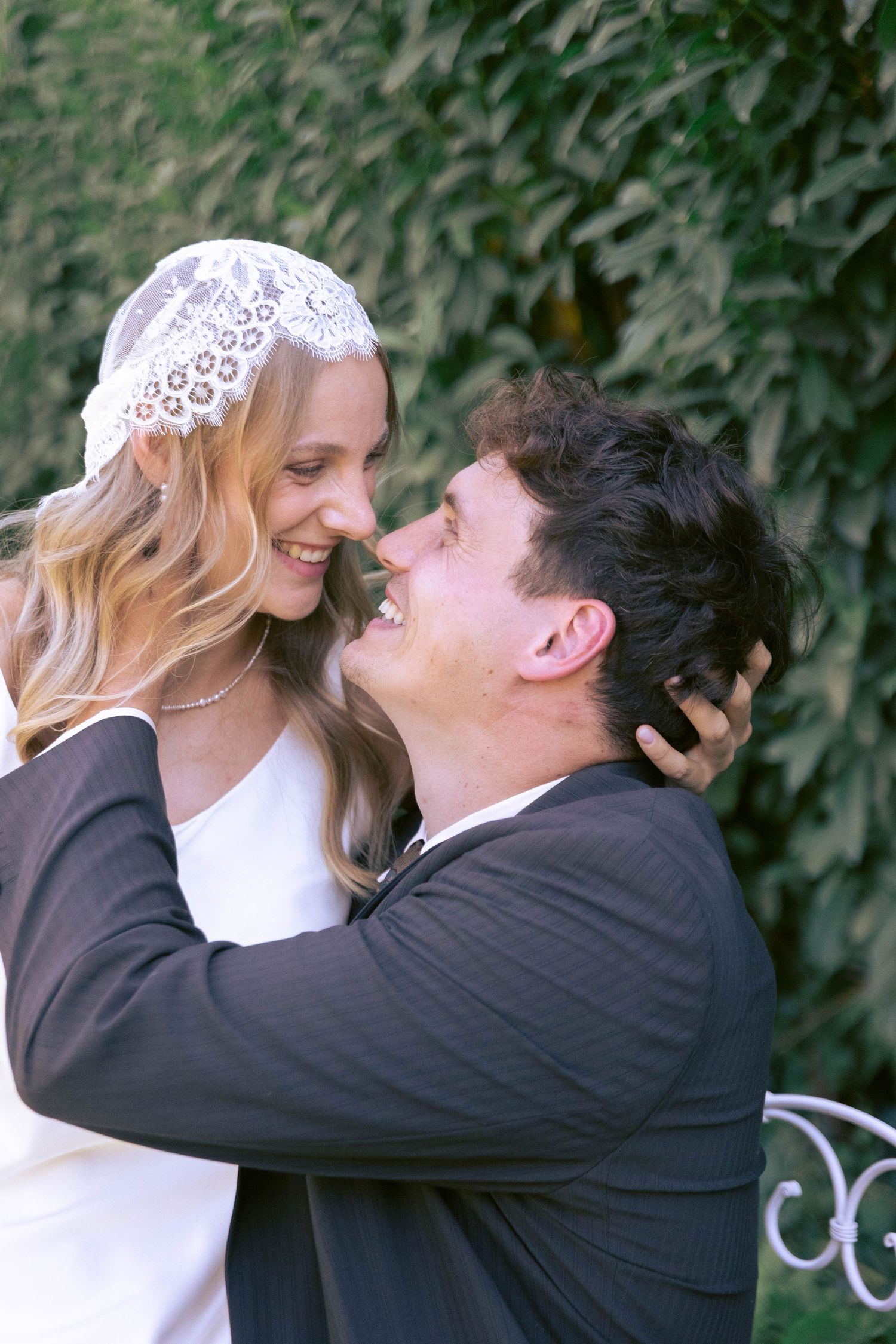 Bride and groom sharing a joyful moment, smiling at each other, bride wearing lace veil, groom in black suit.