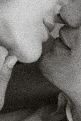 Close-up black and white photo of two people sharing an intimate kiss, captured in soft grainy monochrome tones.