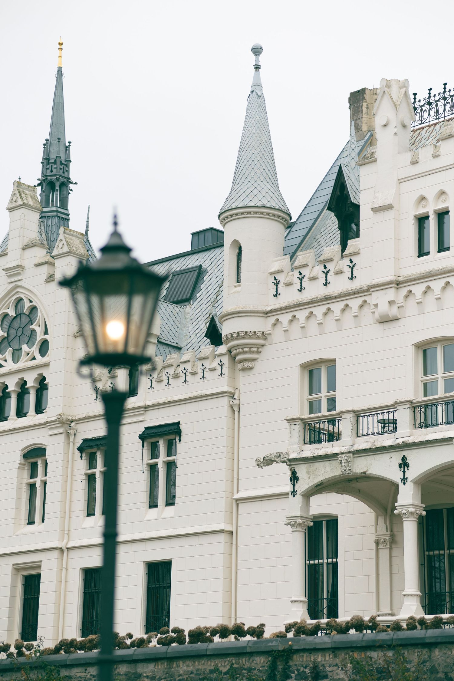White Gothic Revival castle with turrets, ornate facade, and vintage street lamp in foreground.