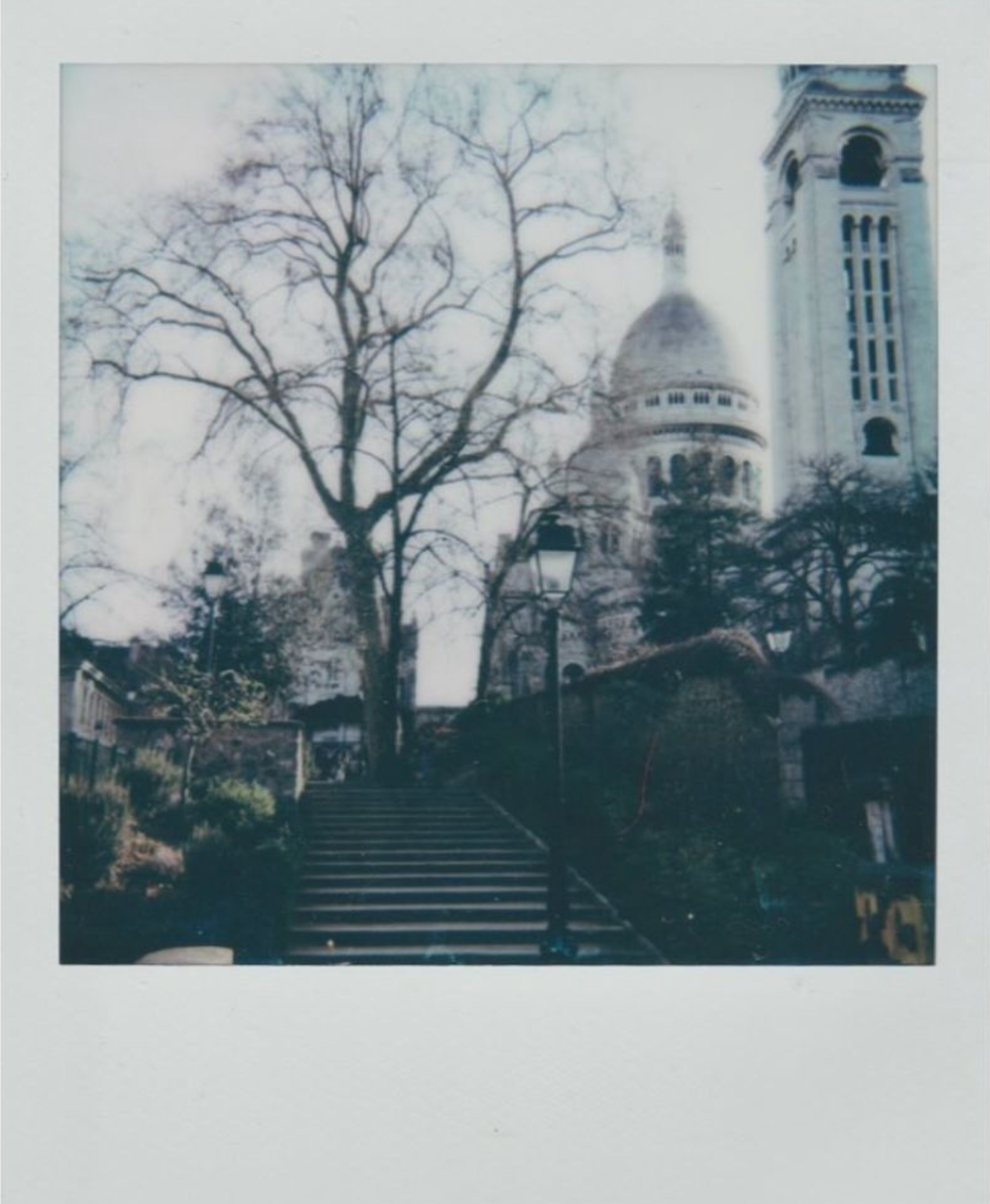 Polaroid photo of Sacré-Cœur Basilica in Paris, viewed from stone steps with bare trees framing the domed cathedral.
