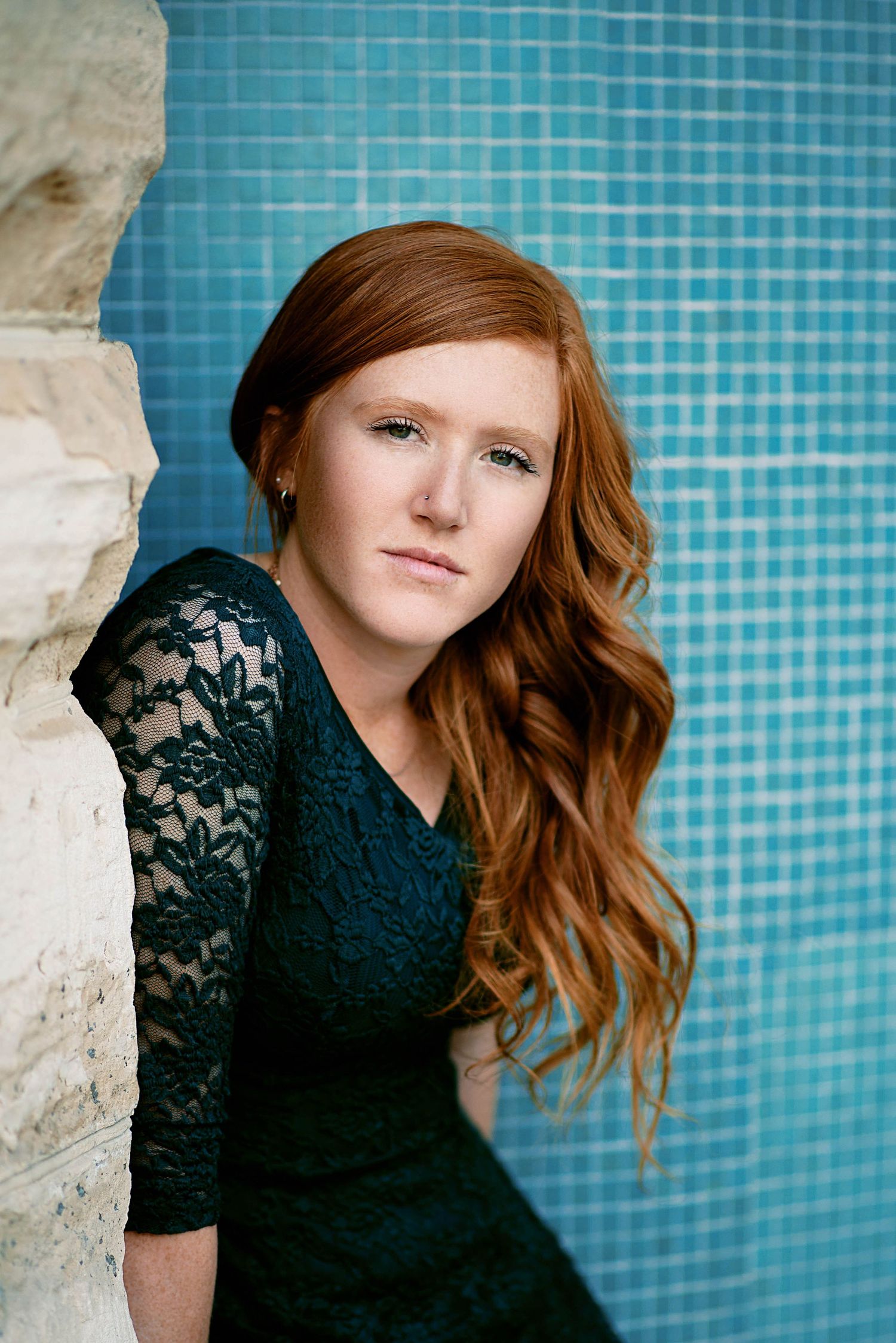 Portrait against turquoise mosaic tile wall featuring someone wearing a black lace dress with flowing red hair.