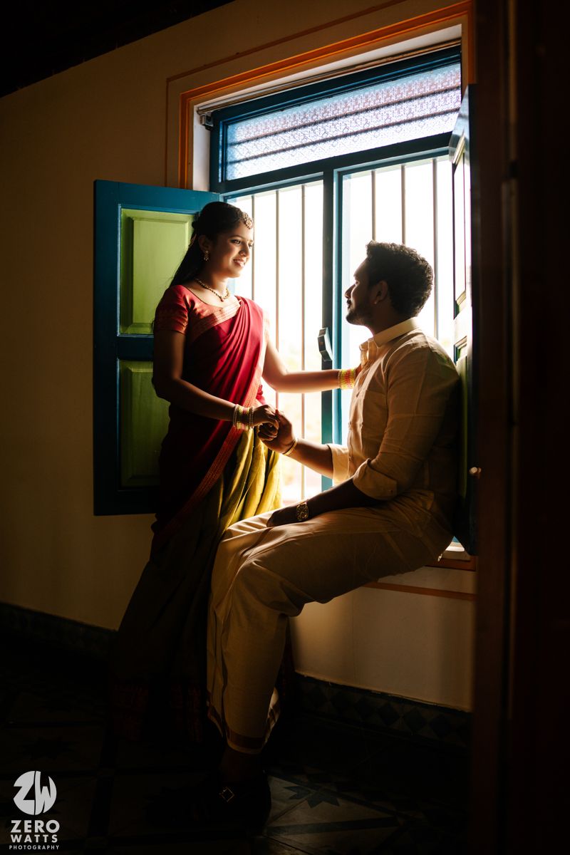 South Indian couple holding hands by a vibrant blue window in dramatic light.