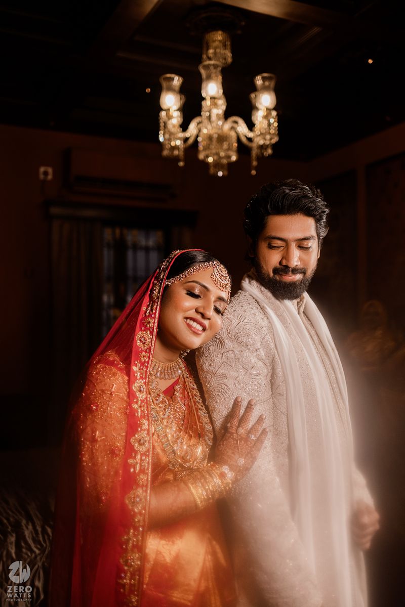 A romantic wedding portrait under a crystal chandelier features traditional Indian wedding attire.