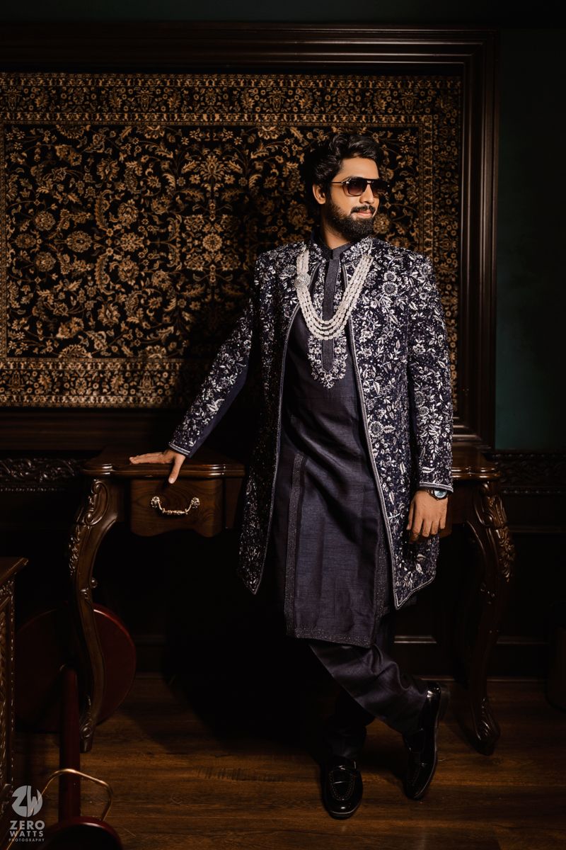 Stylish fashion photoshoot featuring elegant black and silver patterned jacket against ornate wallpaper background.