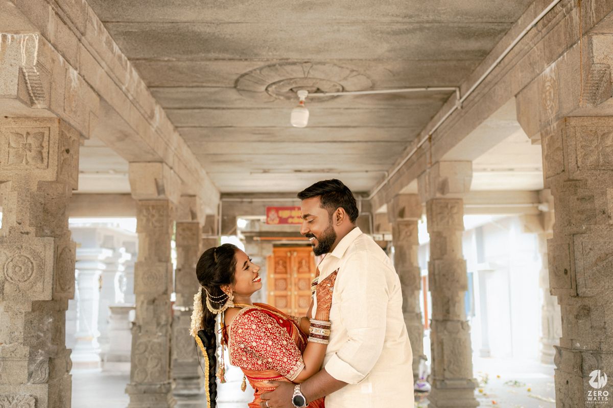 A couple shares a romantic moment in a sunlit temple corridor with ornate stone pillars and architecture.
