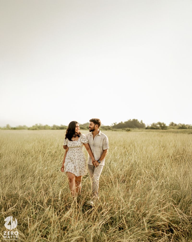 Couple shares intimate moment while standing together in a rustic meadow with warm lighting.