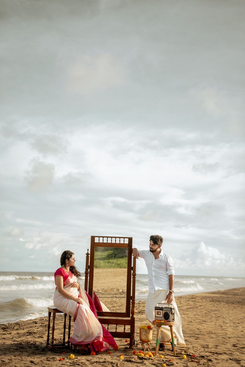 Romantic beach scene with vintage wooden mirror and scattered flowers on sandy shore.
