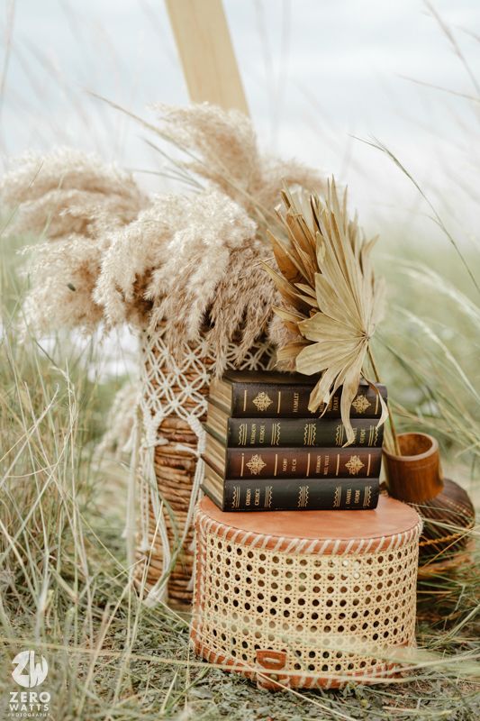 Vintage books and dried pampas grass arranged in a woven basket create a rustic bohemian still life display.