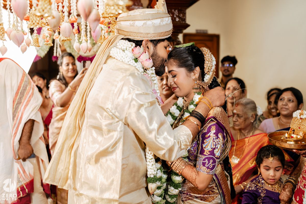 Wedding celebration indoors with guests in traditional Indian attire under elegant decor and lighting.