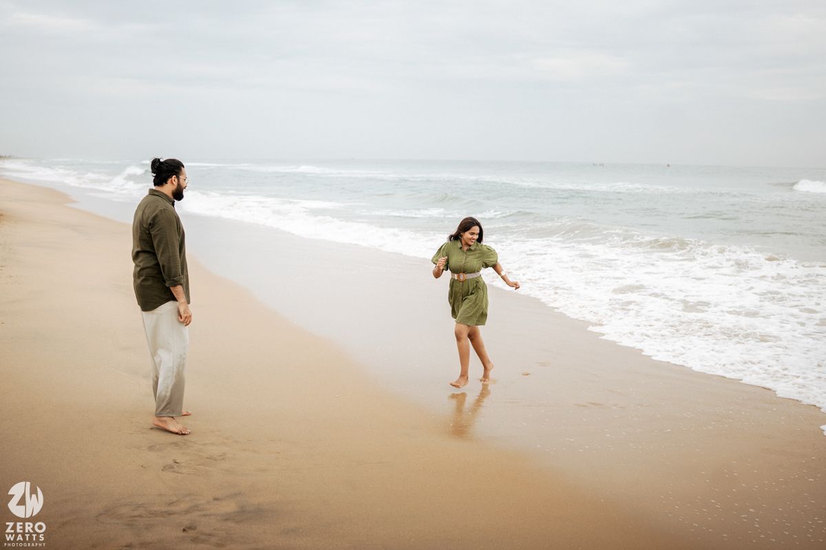 Two people walk and run along a sandy beach with ocean waves in the background.