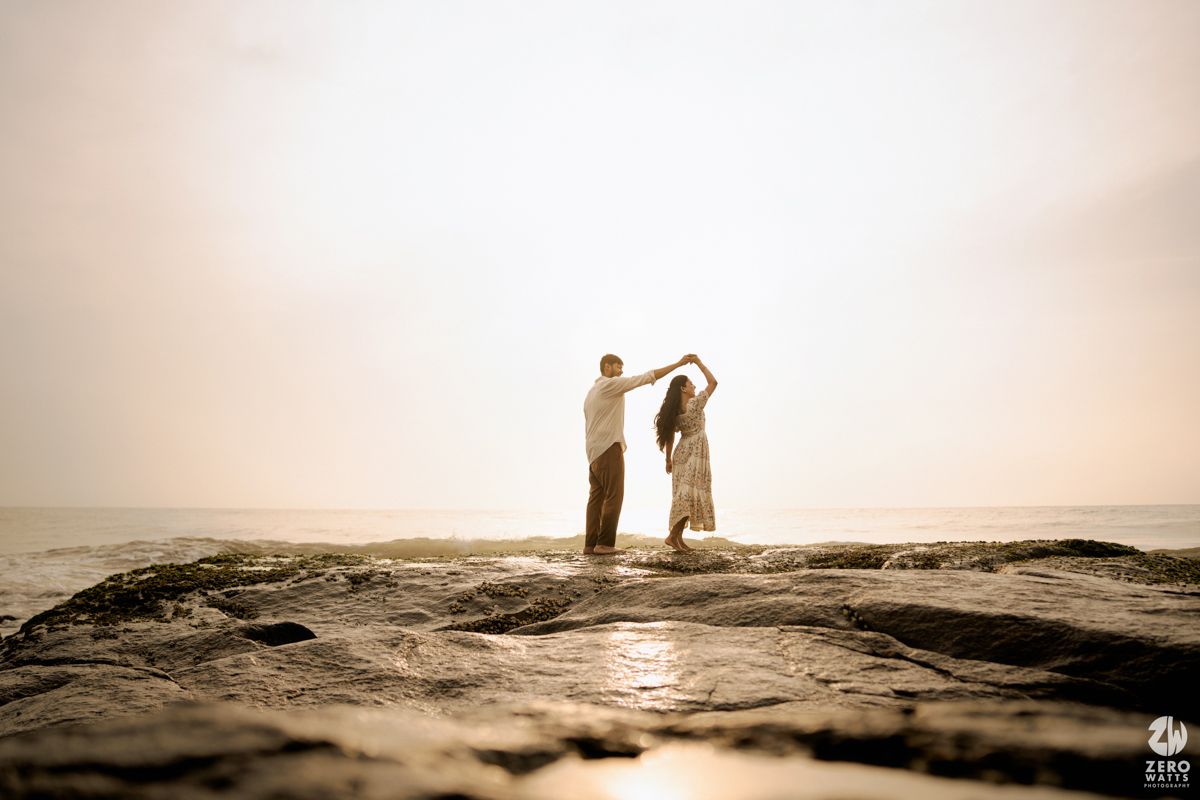 Silhouetted couple dancing together on coastal rocks at sunset with ocean backdrop.