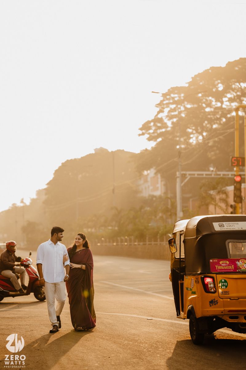 Couple posing near auto rickshaws during golden hour with mosque in background.