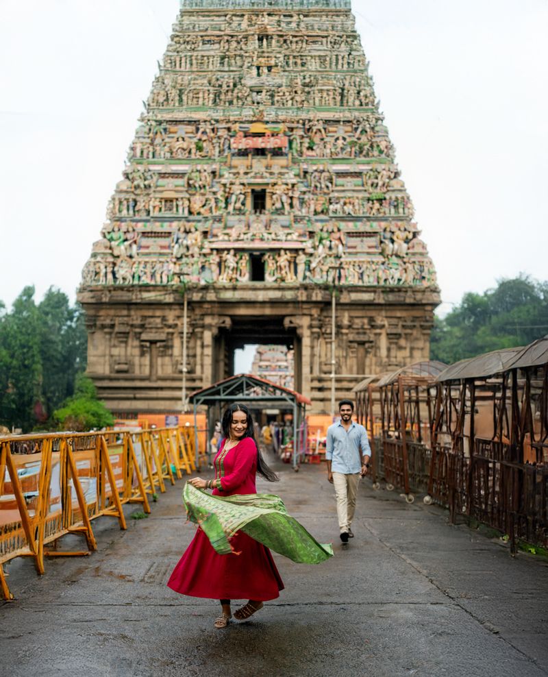 A couple dances and twirls on a bridge walkway in front of an ornate Indian temple gopuram.