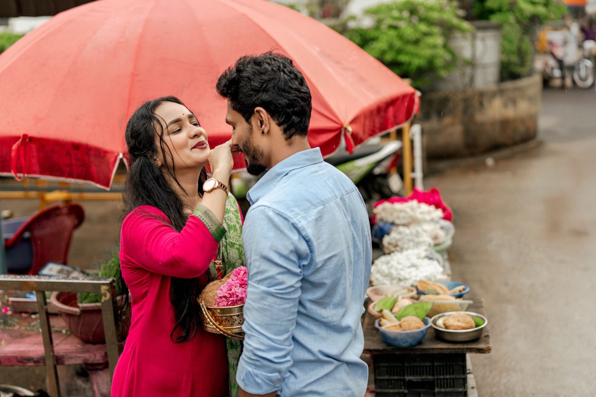A romantic couple shares intimate moments under red umbrellas on a rainy day in an outdoor setting.