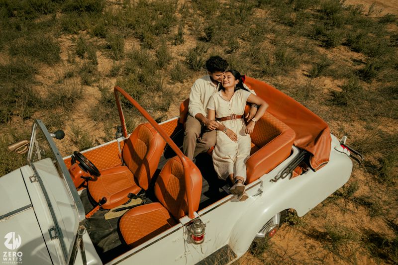 A classic white convertible car with orange leather interior sits in a desert landscape.