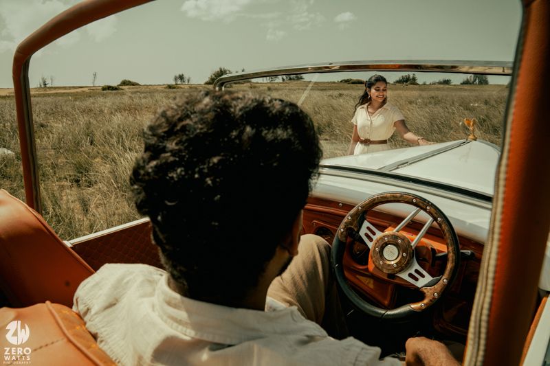 View through vintage car windshield showing cream-colored vehicle interior and steering wheel in rural setting.