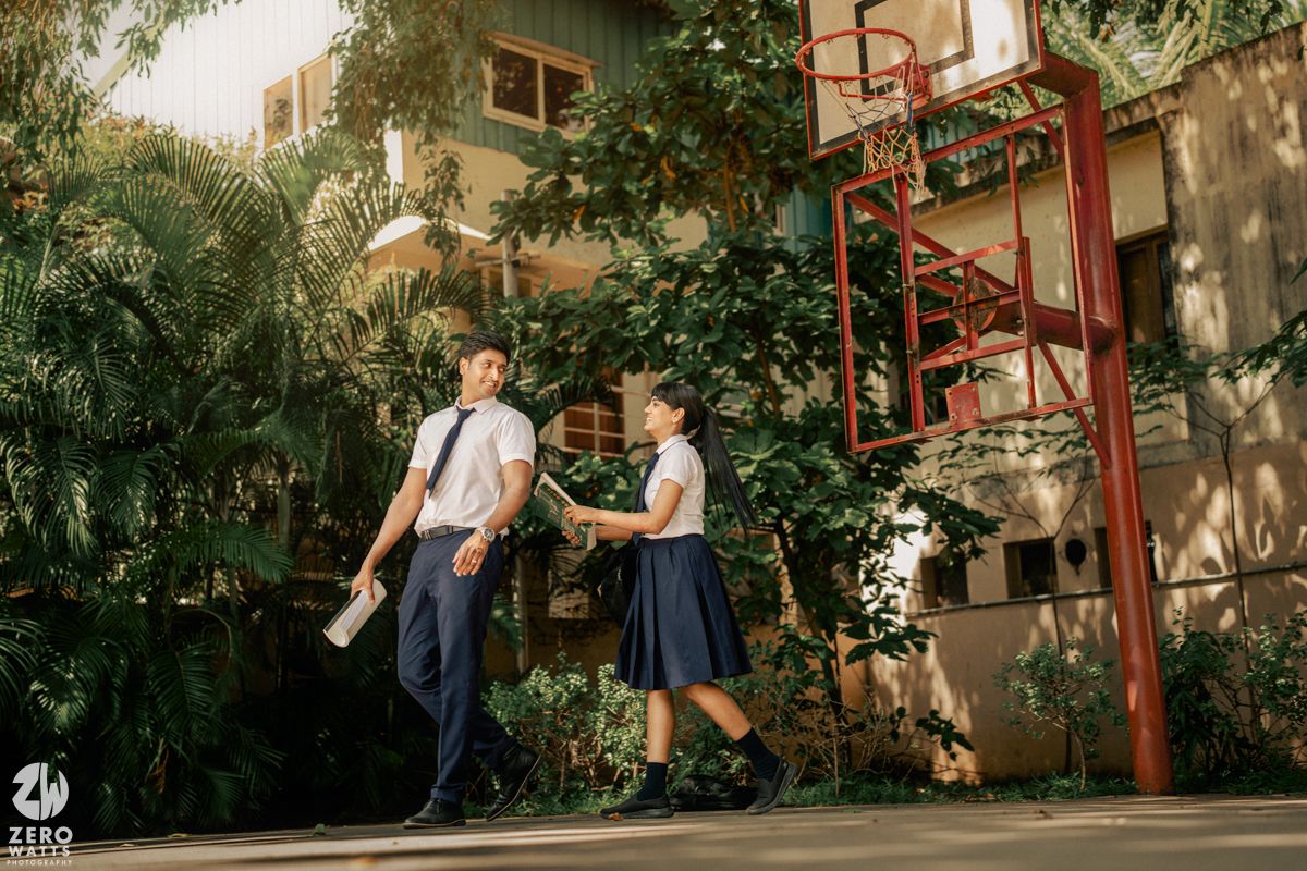 Students in uniforms walk past a basketball court in a garden setting.