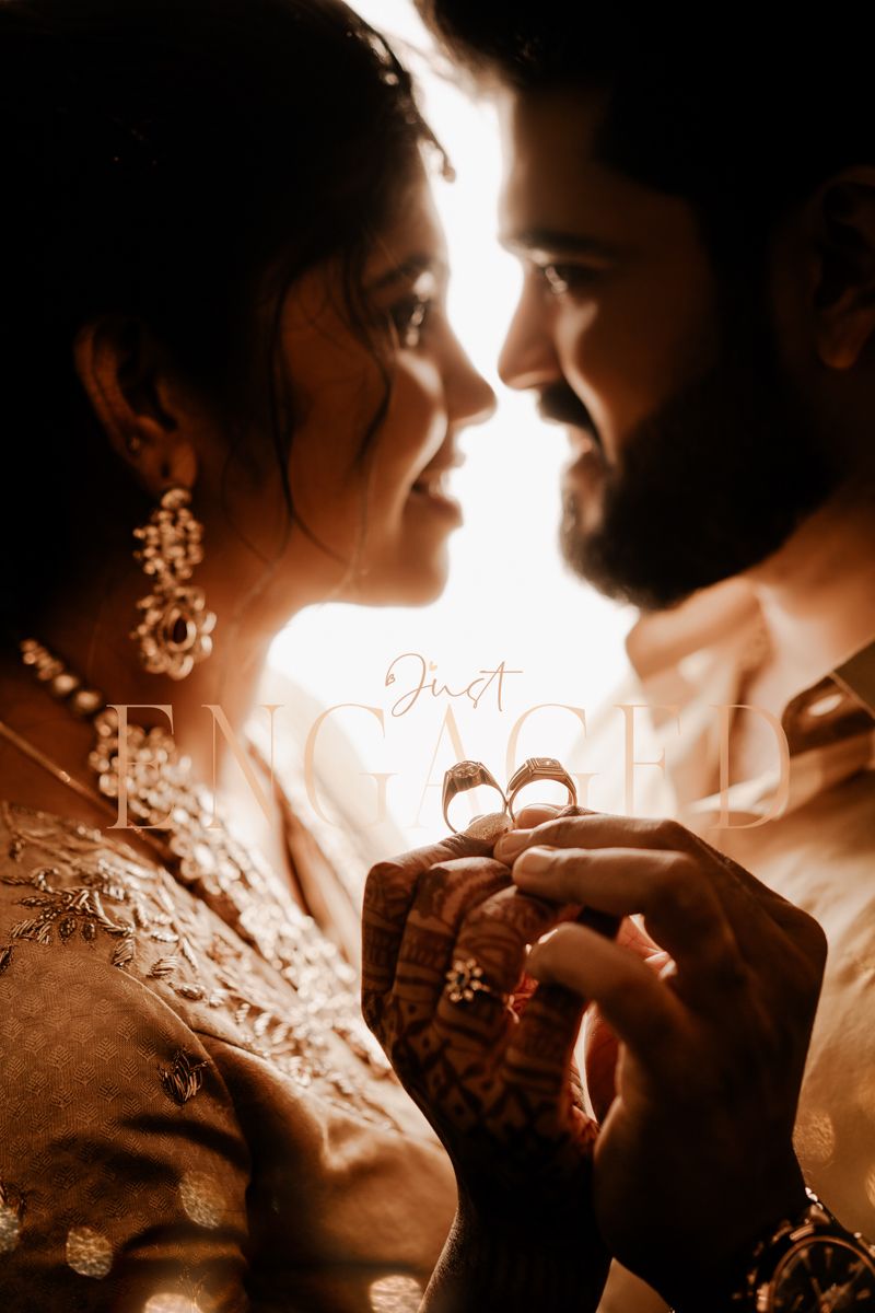 A romantic sepia-toned photograph showing hands gently holding up wedding rings in warm lighting.