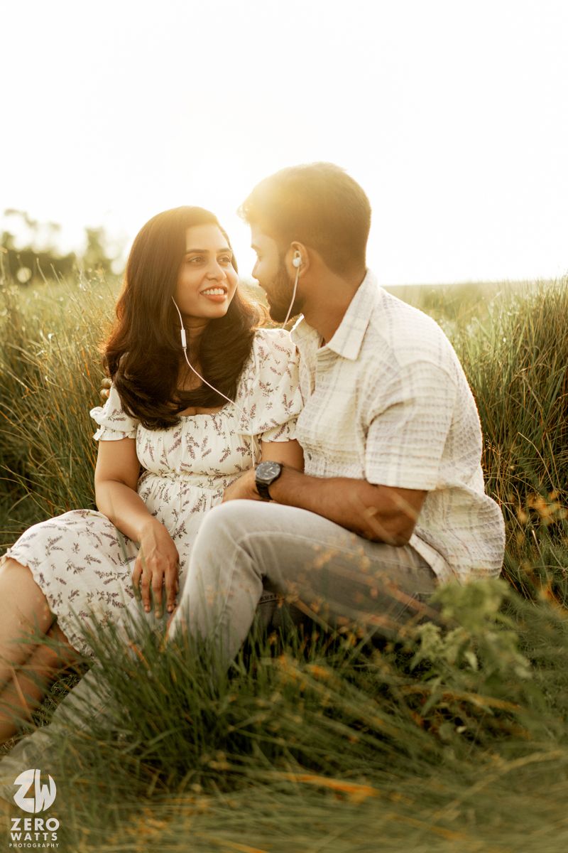 Couple sitting in sunlit meadow share tender moments while wearing coordinated white outfits.