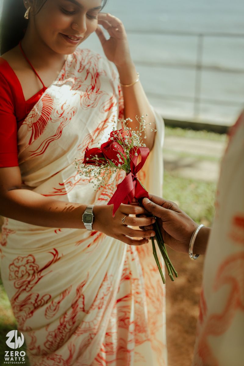 A delicate red and white floral bouquet being presented in a romantic outdoor setting by the sea.
