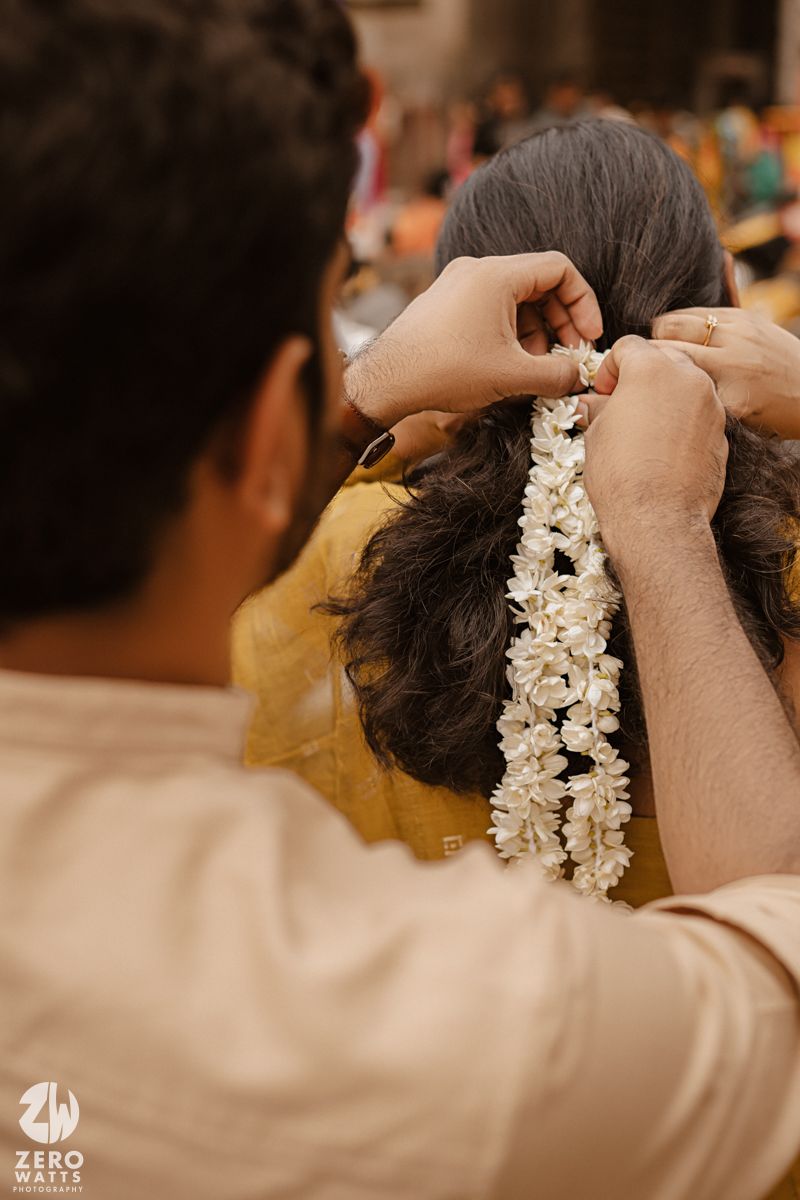 Close-up sequence showing hands placing a delicate white floral garland in dark hair during a traditional ceremony.