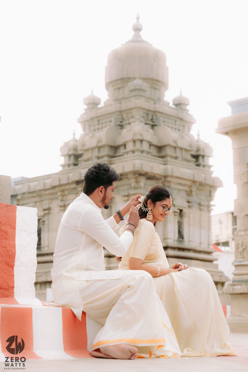 People in light colored clothing photographed against ornate stone architecture with domed structures and pillars.
