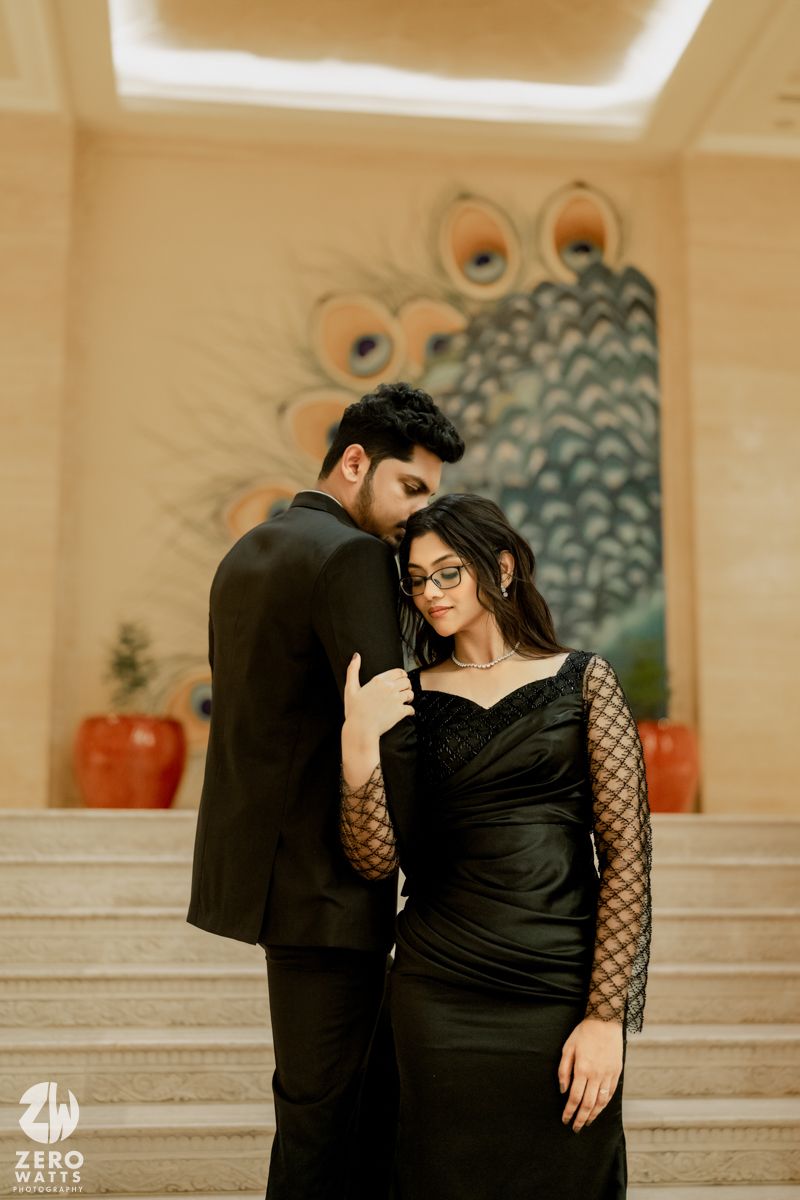 A romantic couple poses against a peacock feather wall design in formal black attire.