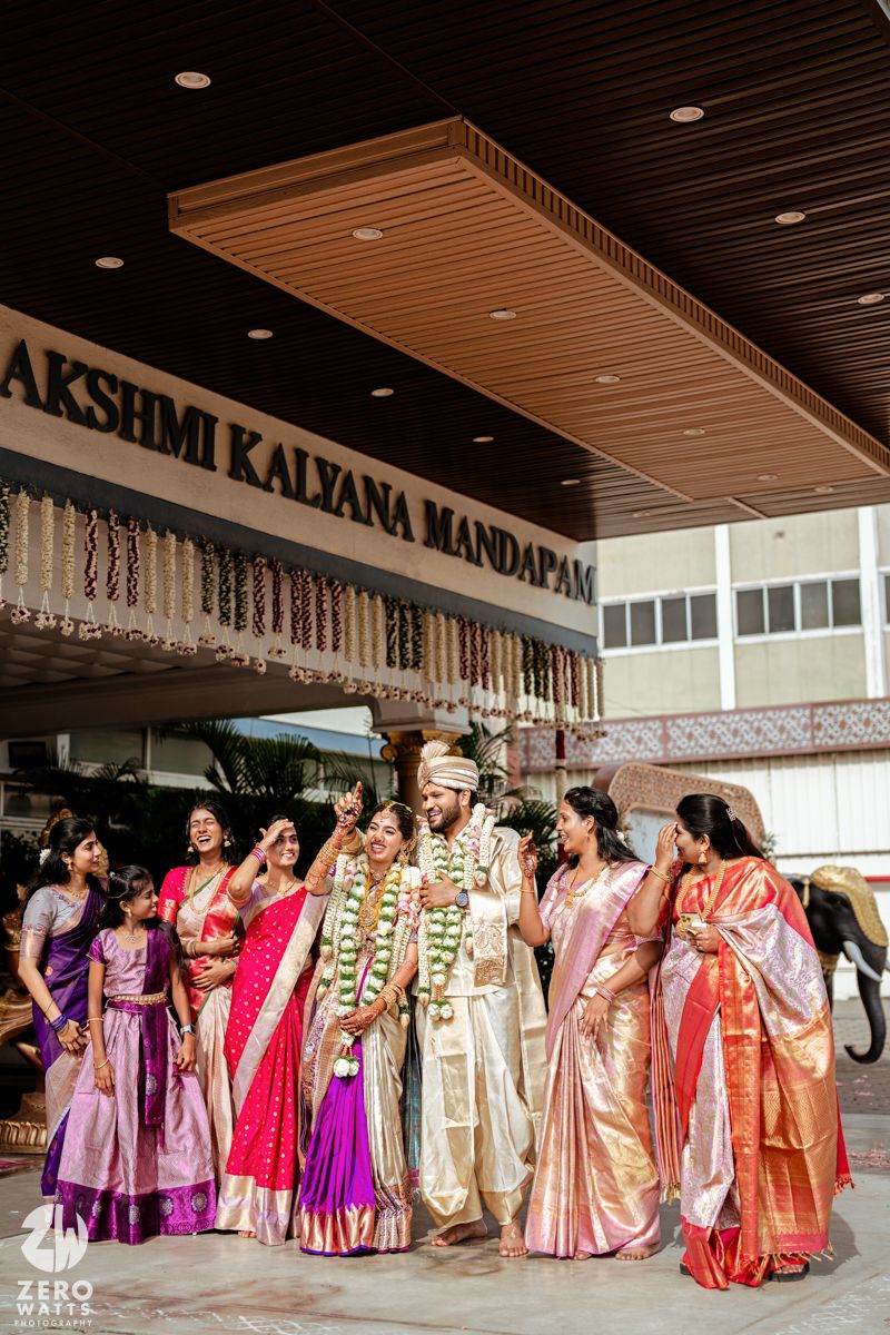 Traditional Indian wedding party in colorful saris and formal attire gathered outside Lakshmi Kalyana Mandapam venue.