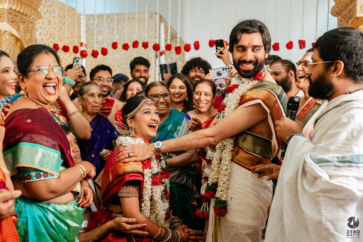Joyful South Indian wedding ceremony with bride in green silk saree and groom exchanging garlands amid smiling guests.